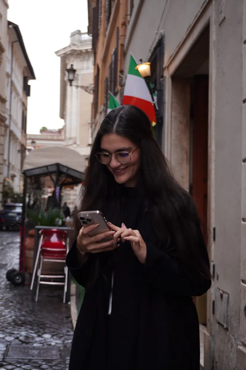 Val revisando su celular y sonriendo en una calle de Roma